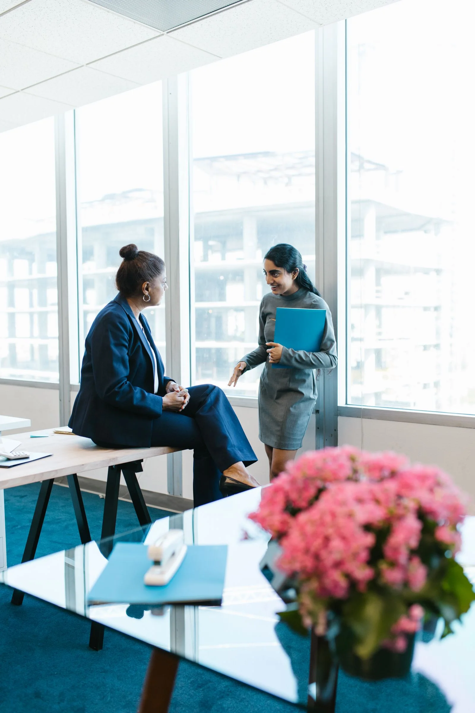 Two professionals in conversation beside an office window.